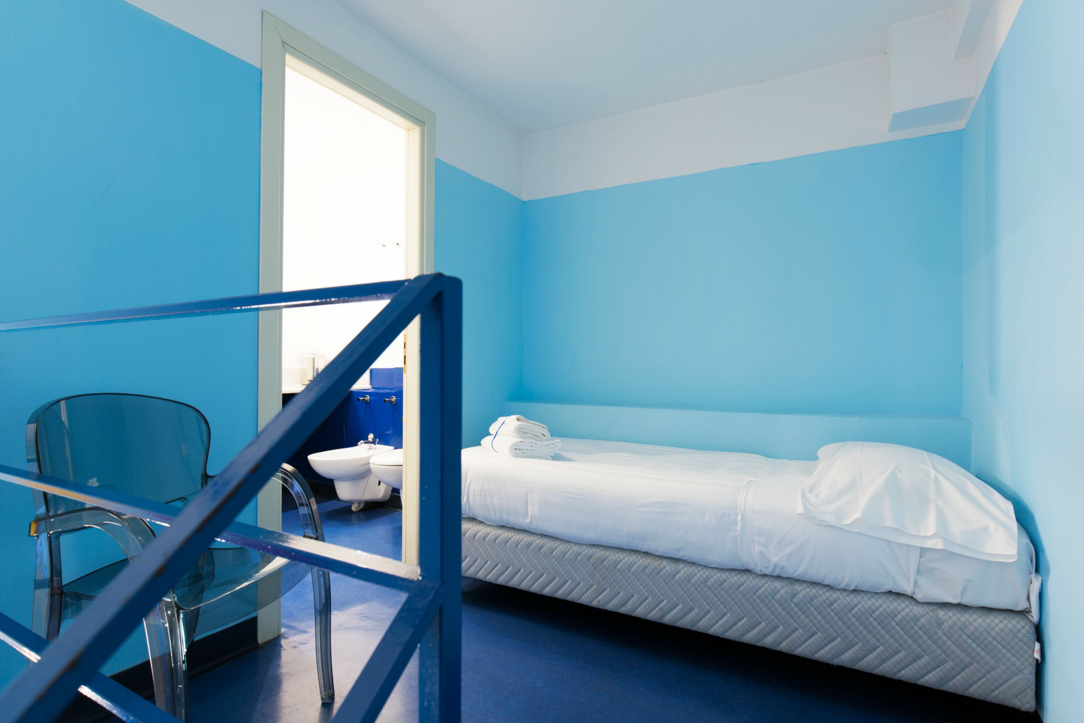 Ein Zimmer mit einem Einzelbett, einem Sessel und einem Fenster.