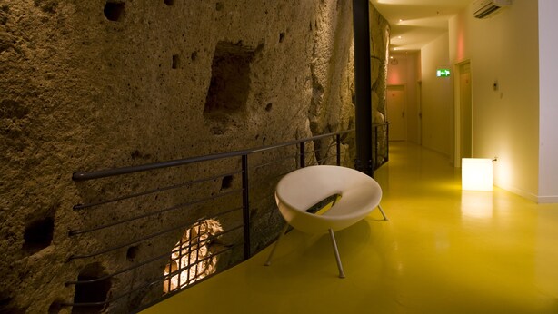 Un pasillo con pared de piedra texturizada, una silla moderna y suelo amarillo.