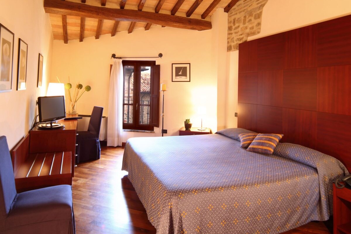 A bedroom with a wooden ceiling, a bed with patterned bedding, a desk with a computer, and a chair.