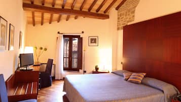 Una camera da letto con soffitto in legno, un letto con biancheria a motivi, una scrivania con un computer e una sedia.