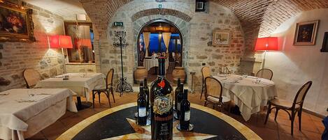 A restaurant with stone walls, round tables, and wine bottles.