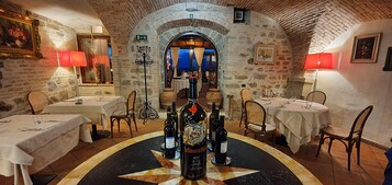 Un restaurante con paredes de piedra, mesas redondas y botellas de vino.
