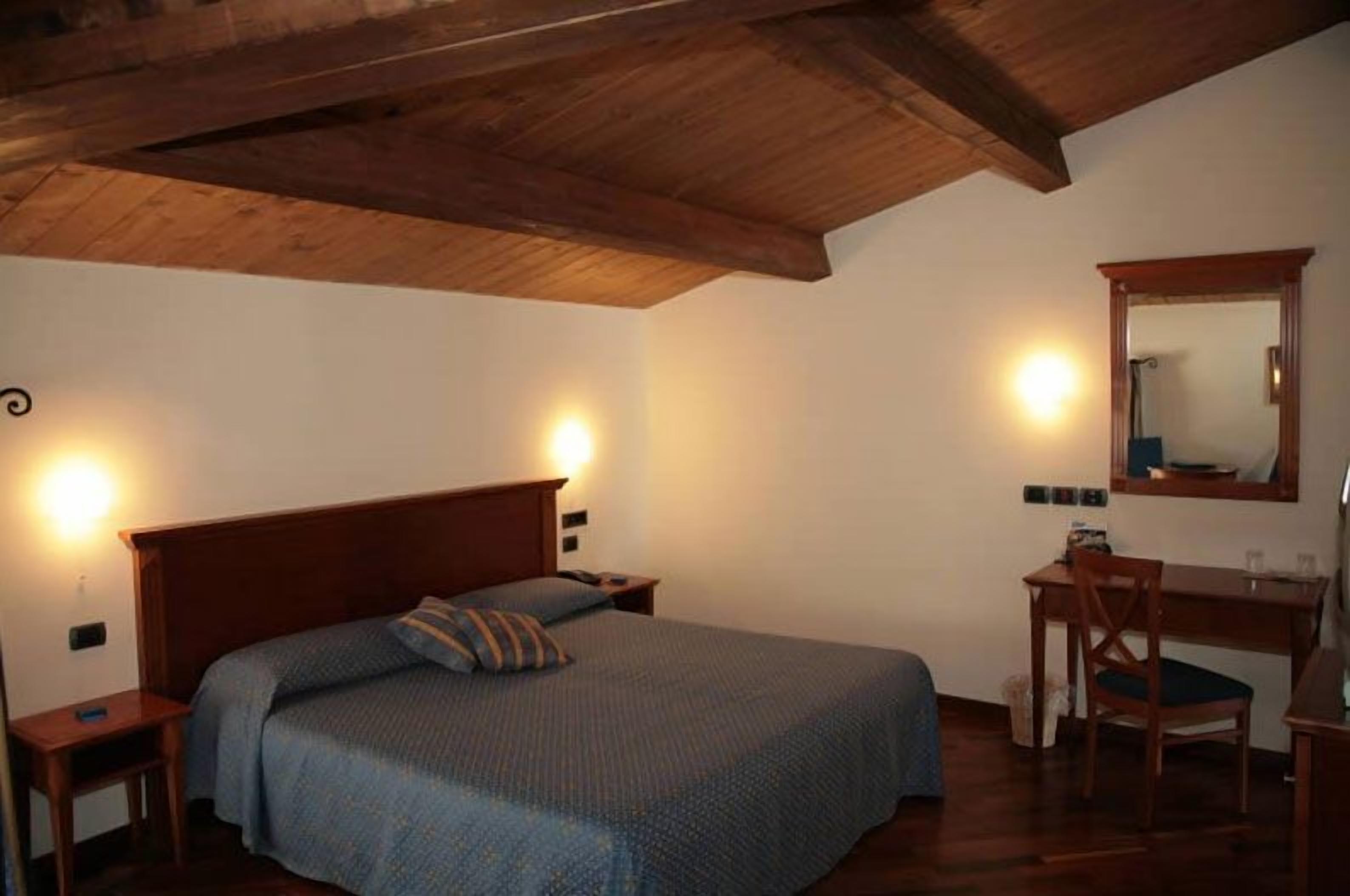 Een slaapkamer met een houten plafond, een bed met een blauwe deken, een bureau met een stoel en een spiegel aan de muur.