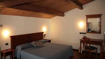 Een slaapkamer met een houten plafond, een bed met een blauwe deken, een bureau met een stoel en een spiegel aan de muur.