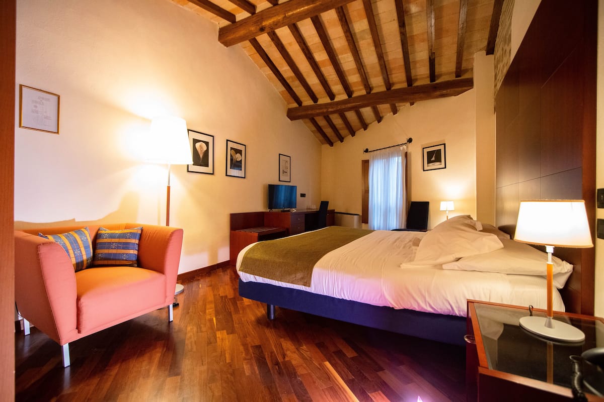 A hotel room with a wooden ceiling, a bed with white bedding, a pink sofa, and a desk with a lamp.