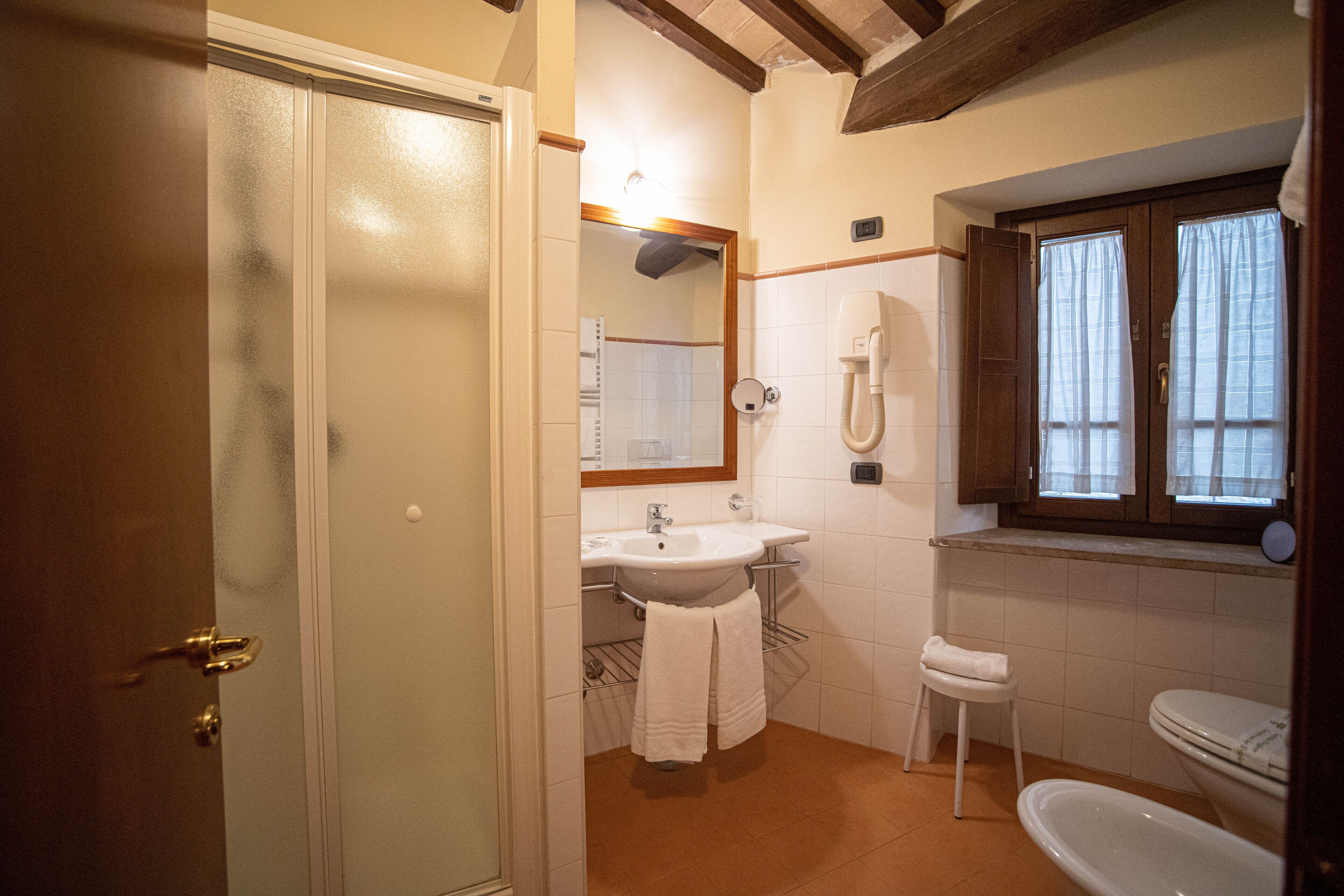 A bathroom with a sink, mirror, toilet, and a window with curtains.