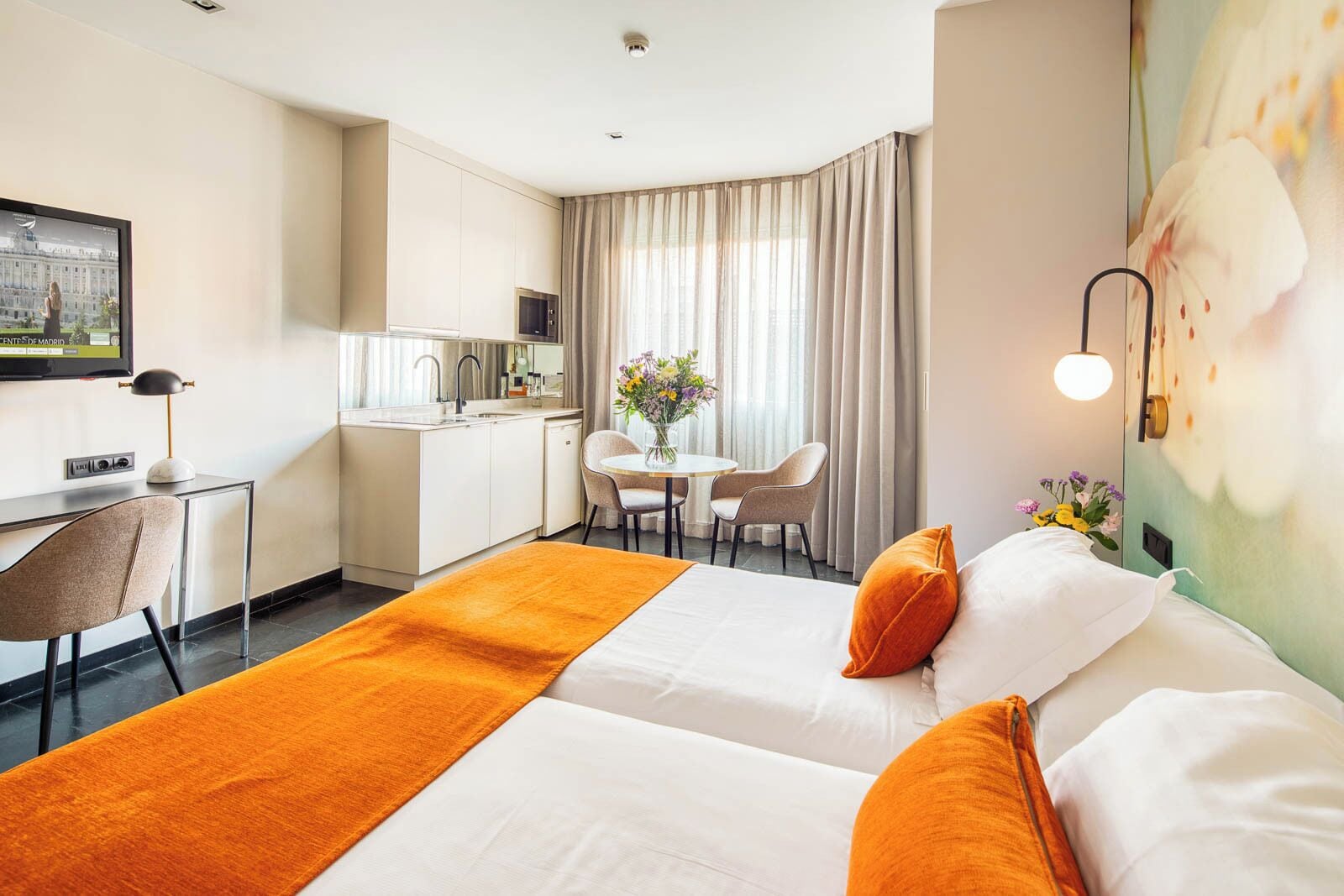 Habitación de hotel con dos camas, un escritorio, una silla, una mesa de comedor y una zona de cocina.