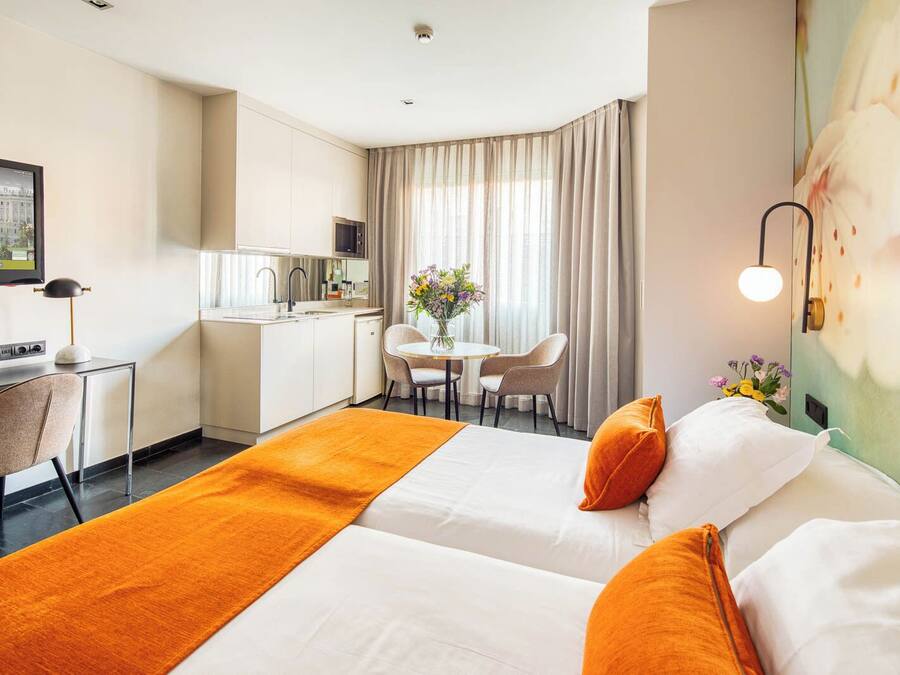 Habitación de hotel con dos camas, un escritorio, una silla, una mesa de comedor y una zona de cocina.