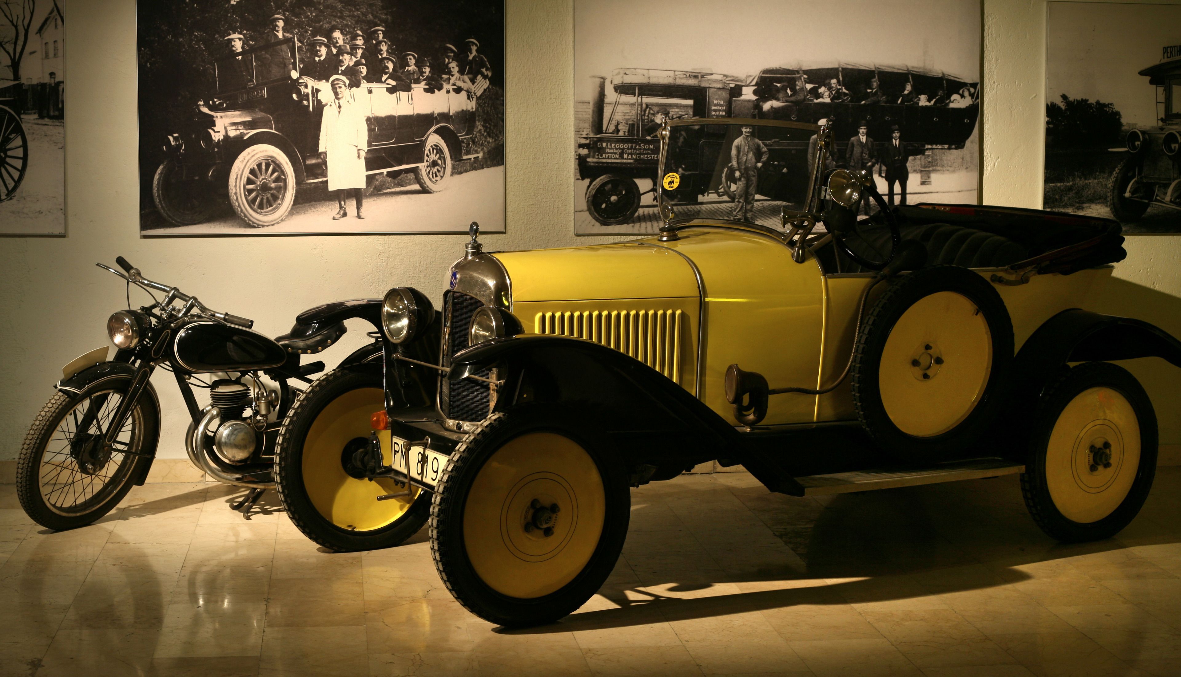 A vintage yellow car and a motorcycle in a museum setting.