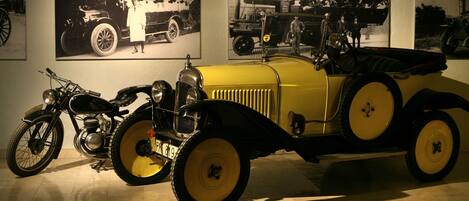 A vintage yellow car and a motorcycle in a museum setting.