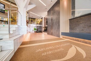 Un moderno vestíbulo de hotel con piso de mármol, un mostrador de recepción y una escalera que sube a un nivel superior.
