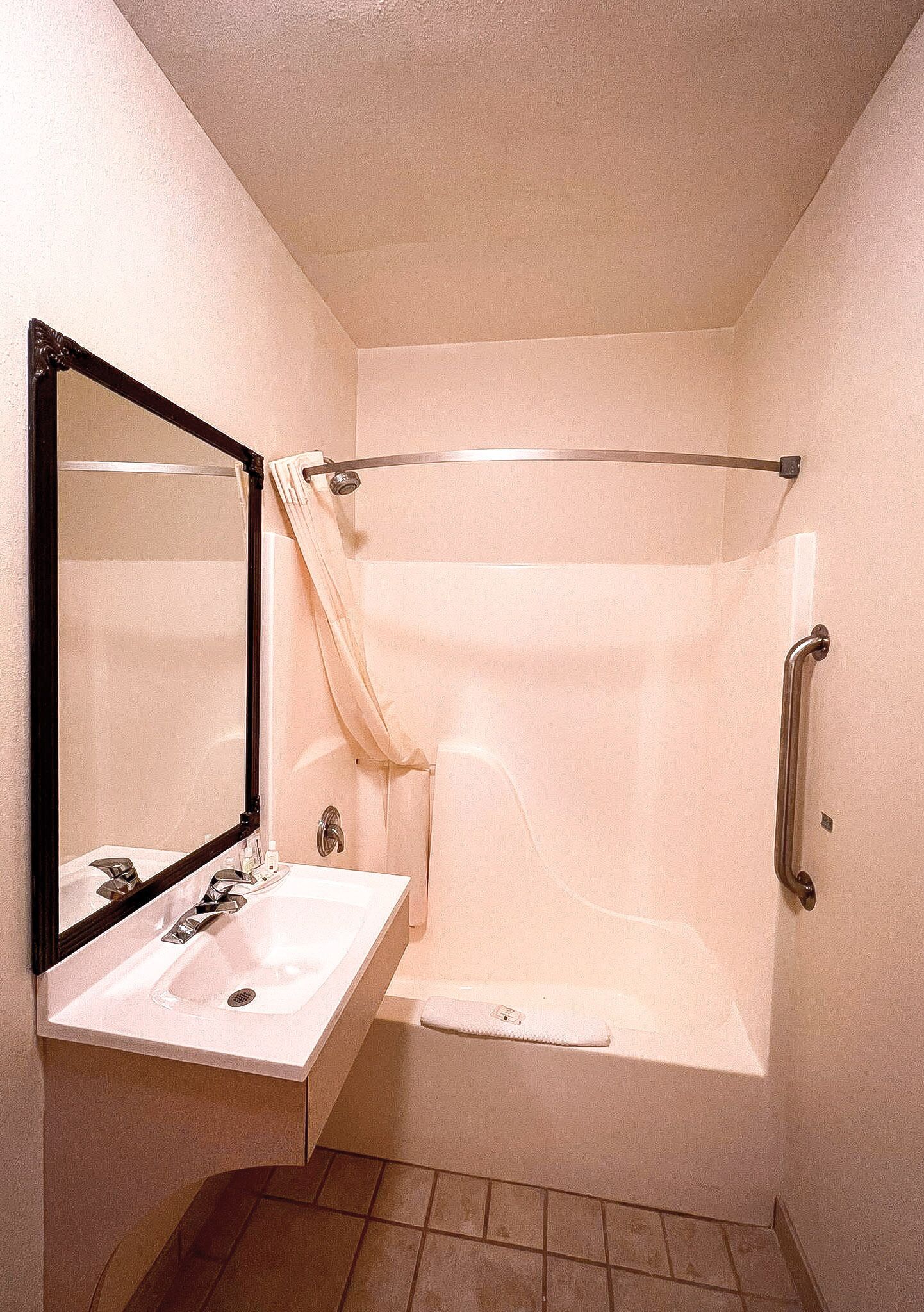 Ein Badezimmer mit einem weißen Waschbecken, einem Spiegel, einer Duschkabine mit Vorhang und einer Haltestange.