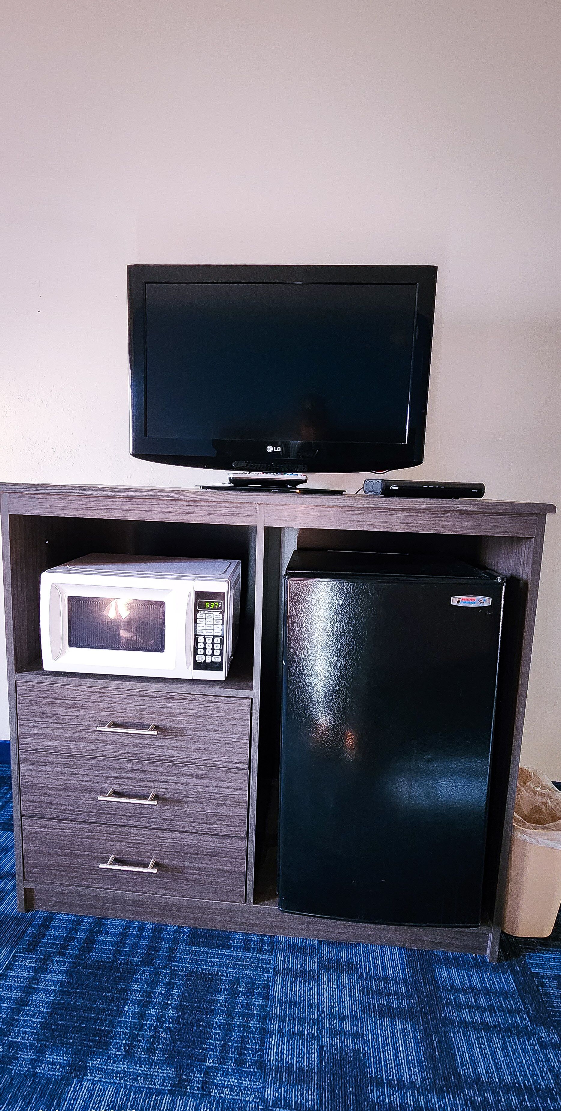 Une petite cuisine équipée comprenant un four à micro-ondes, un réfrigérateur et un téléviseur à écran plat, le tout installé sur un meuble en bois.