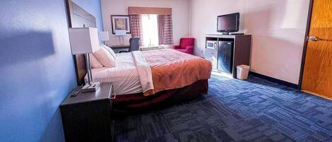 Quarto de hotel com cama, escrivaninha, televisão e lixeira.