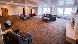 A spacious lobby with a patterned carpet, seating area with chairs and a sofa, a fireplace, and large windows providing natural light.