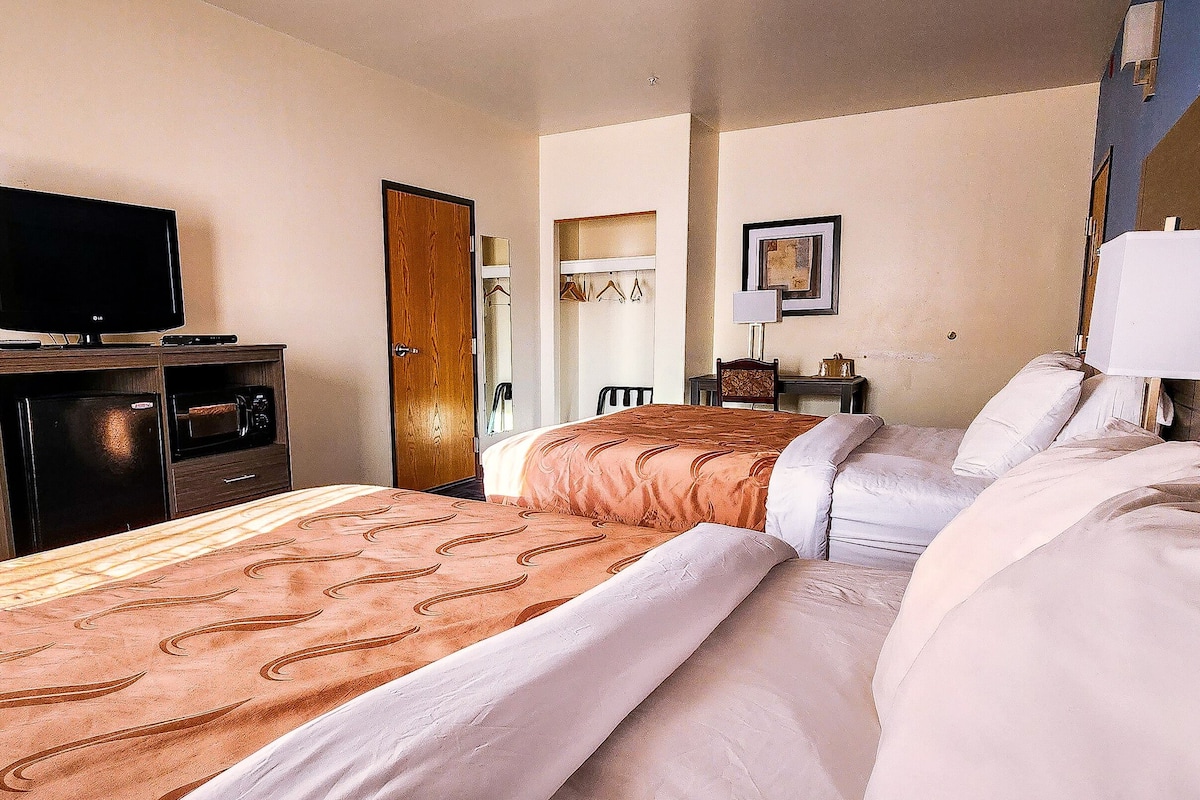 Quarto de hotel com cama, televisão em suporte, guarda-roupa e espelho na parede.