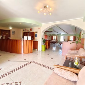 A hotel lobby with a reception desk, seating area, and a dining space. - Hotel Alex (Karpathos)