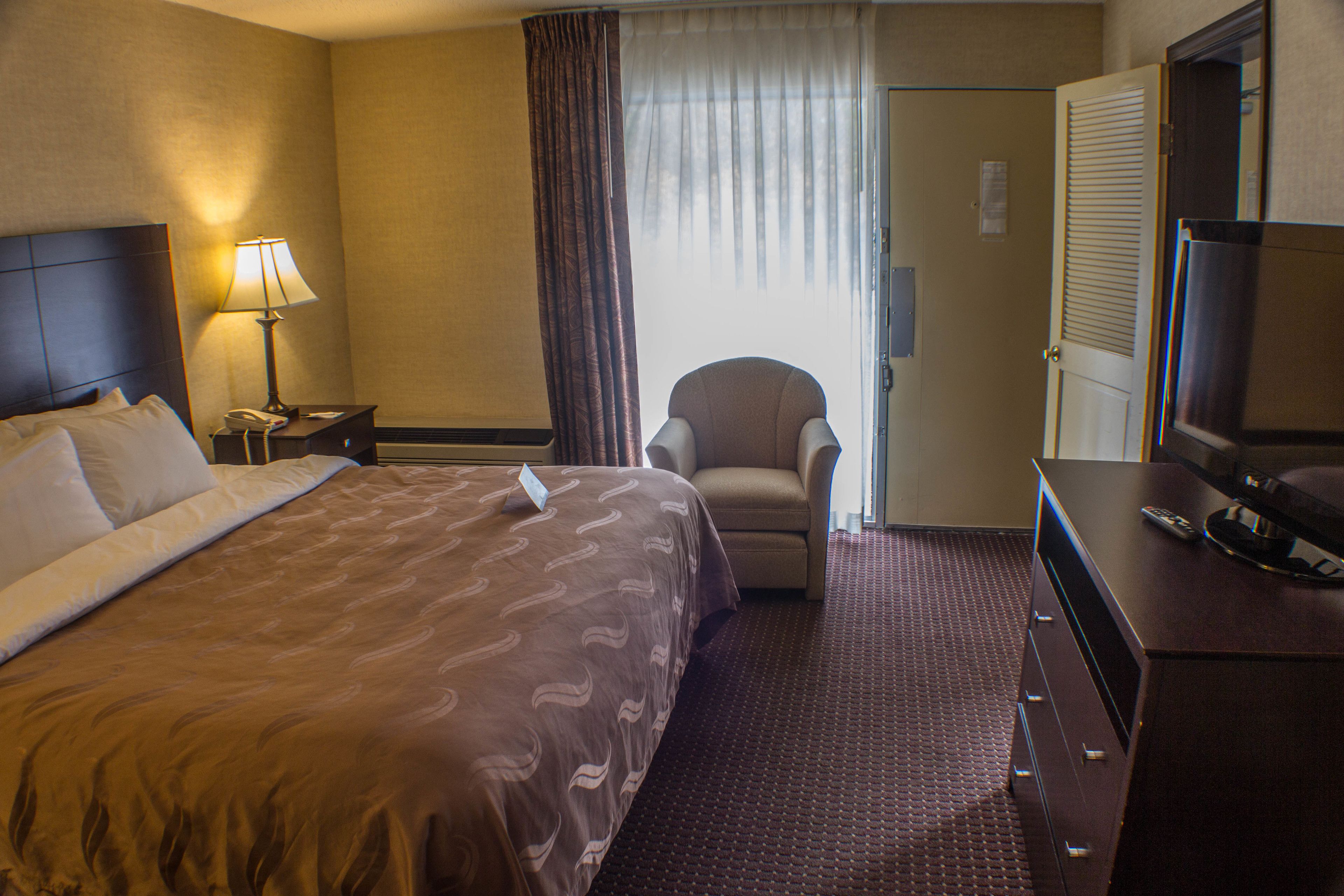 Une chambre d’hôtel avec un grand lit, une chaise, un bureau avec une télévision et une porte.