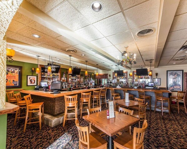 A bar area with wooden chairs and tables, a counter with a TV, and a patterned carpet.