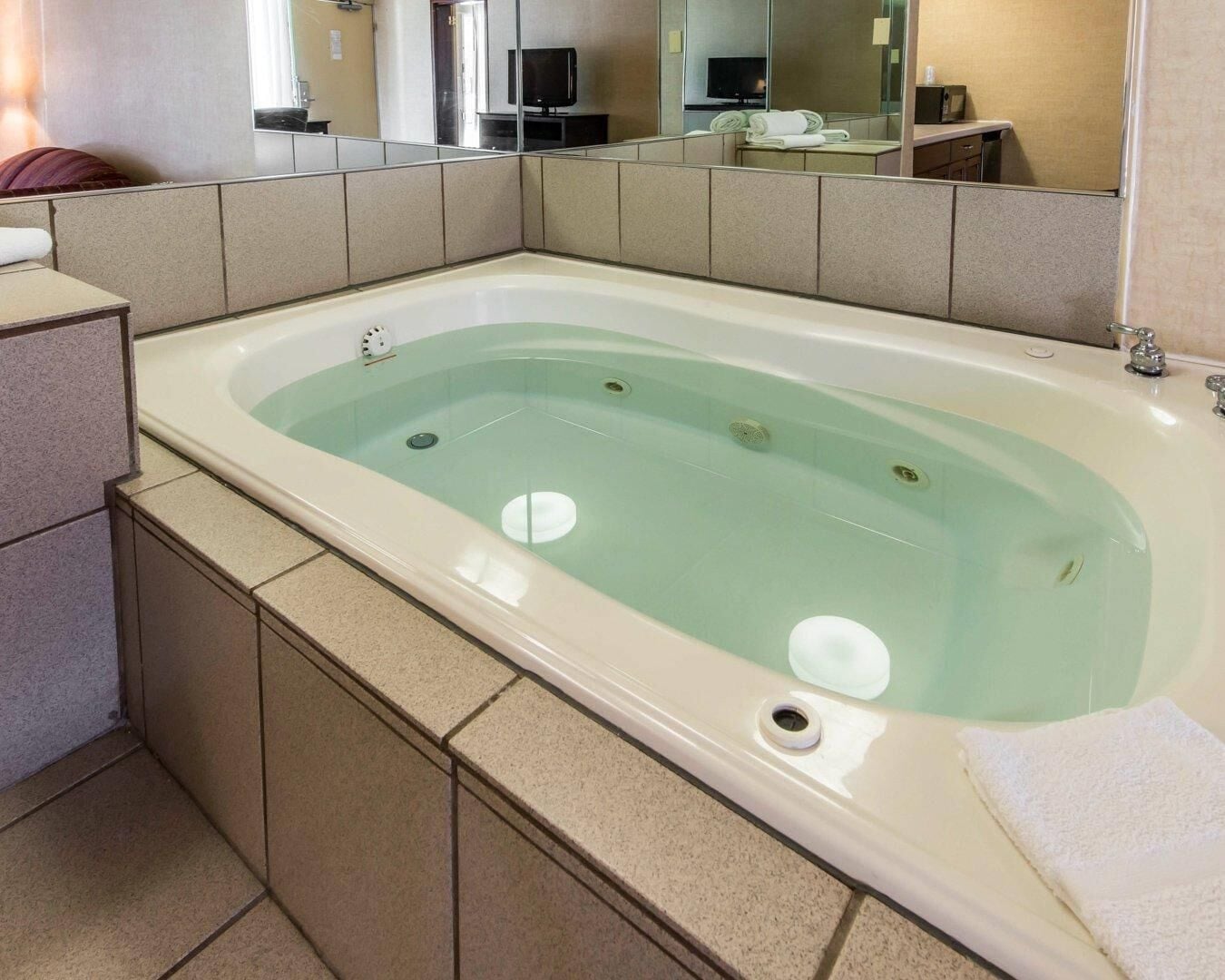 A large bathtub with a glass panel, a sink, and a mirror above it.
