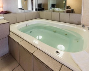 A large bathtub with a glass panel, a sink, and a mirror above it.