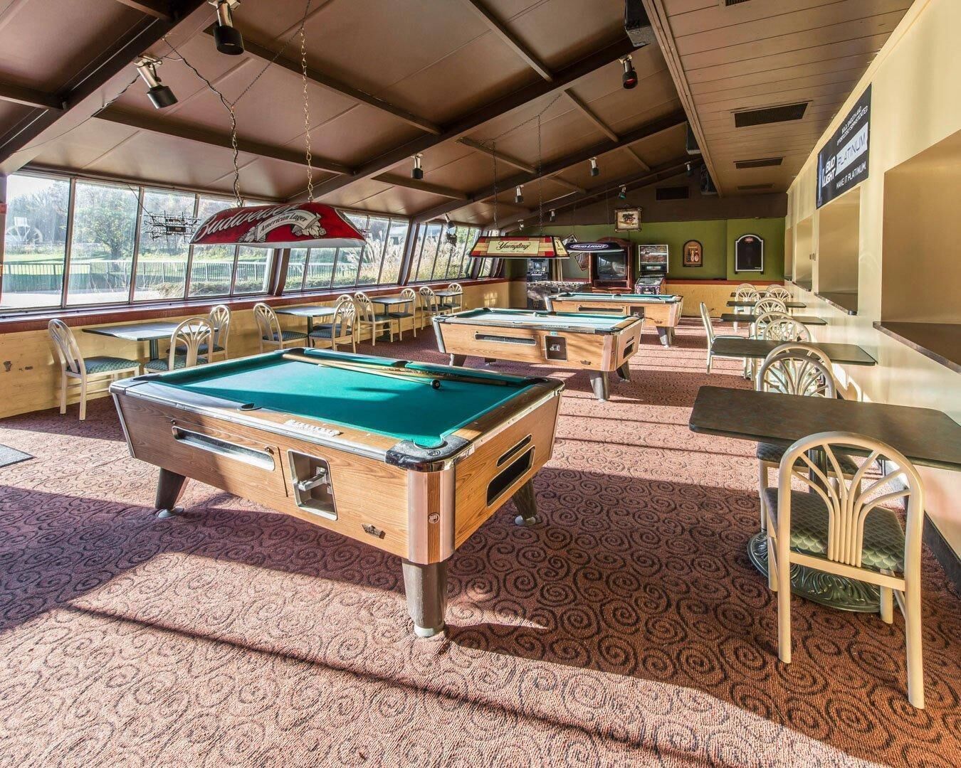 A pool hall with multiple pool tables, chairs, and a large window with a view.