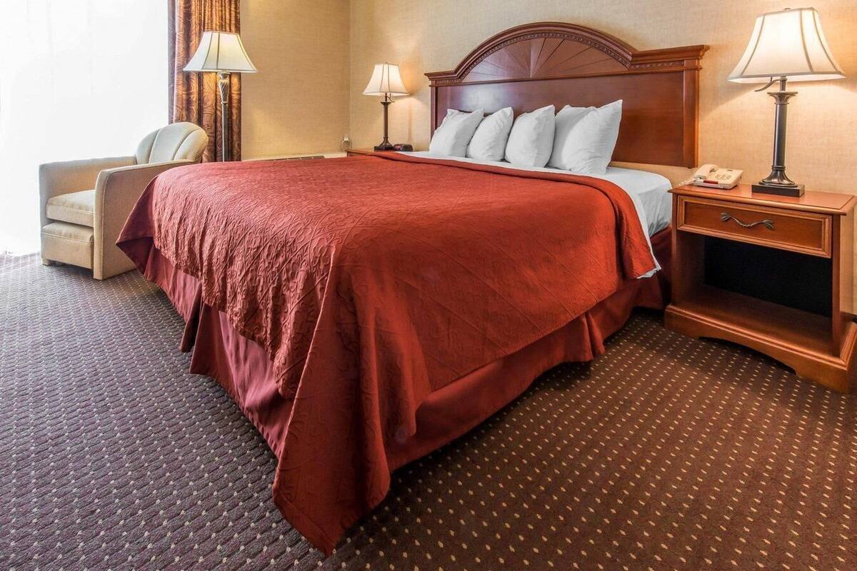 A hotel room with a large bed, two bedside tables, a chair, and a carpeted floor.