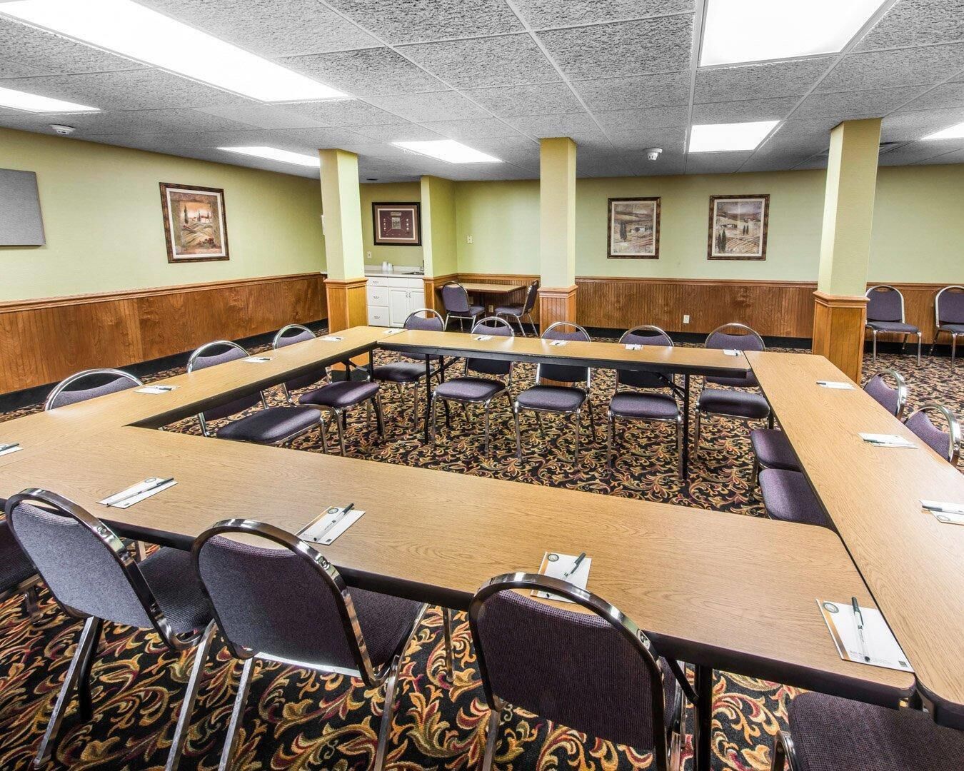 A conference room with a long table and chairs, a patterned carpet, and framed pictures on the walls.