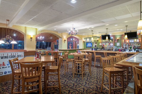 A restaurant with wooden tables and chairs, a bar area with a variety of bottles, and a sign advertising a wing cook-off.