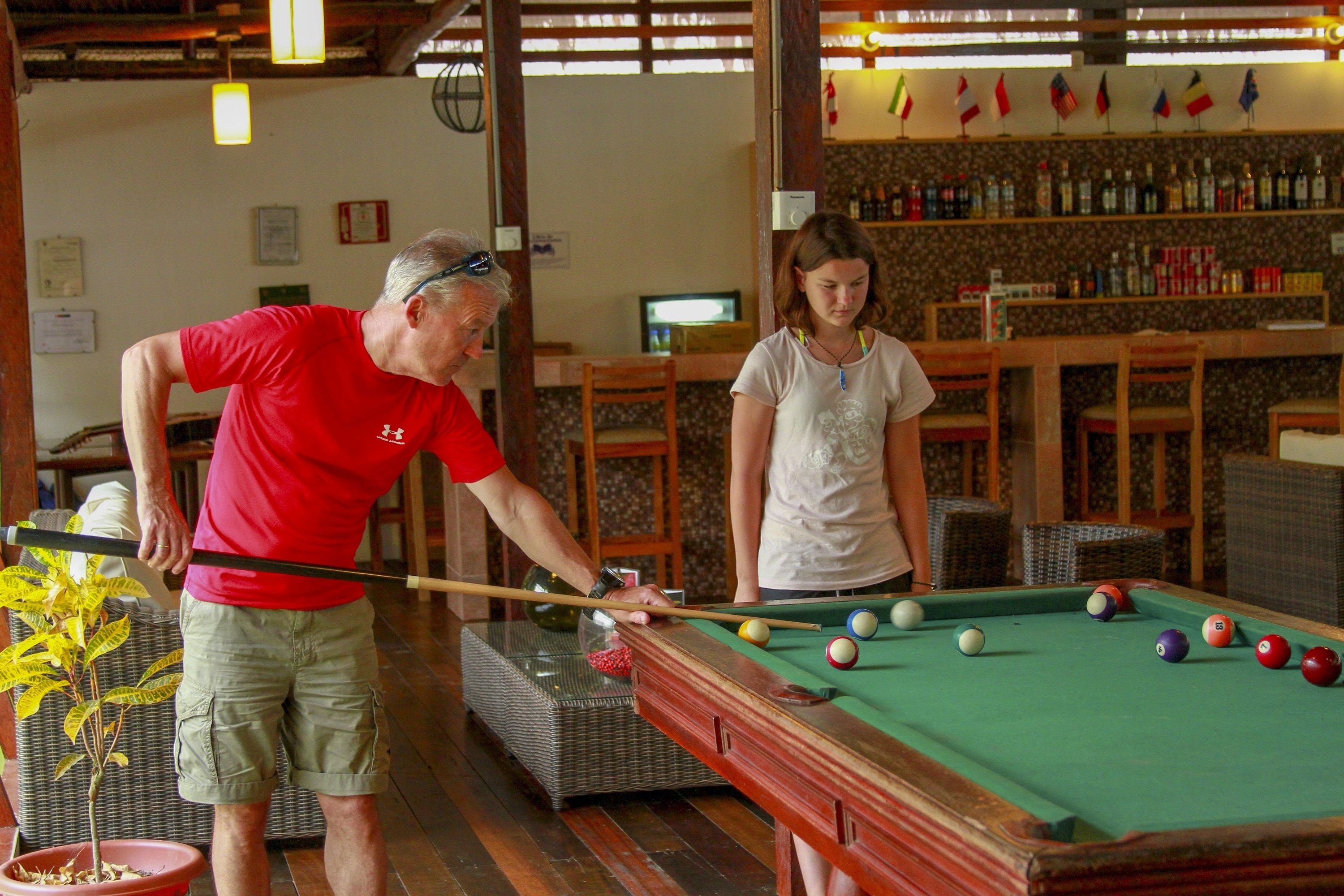 A pool table in a room with wicker furniture and a bar area with flags.