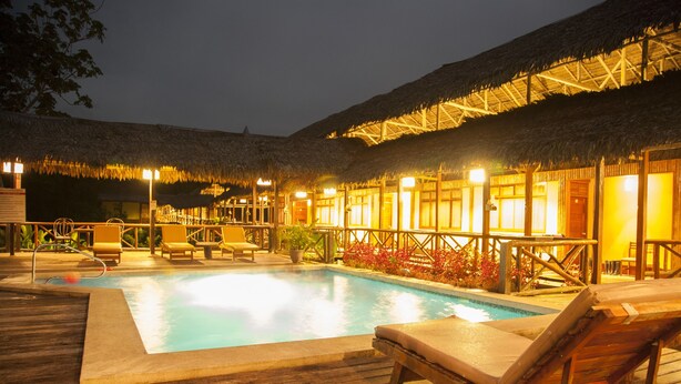 A wooden deck with a pool, lounge chairs, and thatched-roof structures. - Heliconia Amazon River Lodge (Indiana)