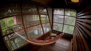 A hammock suspended between two large windows overlooking a wooden deck. - Heliconia Amazon River Lodge (Indiana)