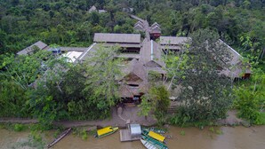 A traditional wooden structure with a thatched roof, surrounded by dense greenery and a river. - Heliconia Amazon River Lodge (Indiana)