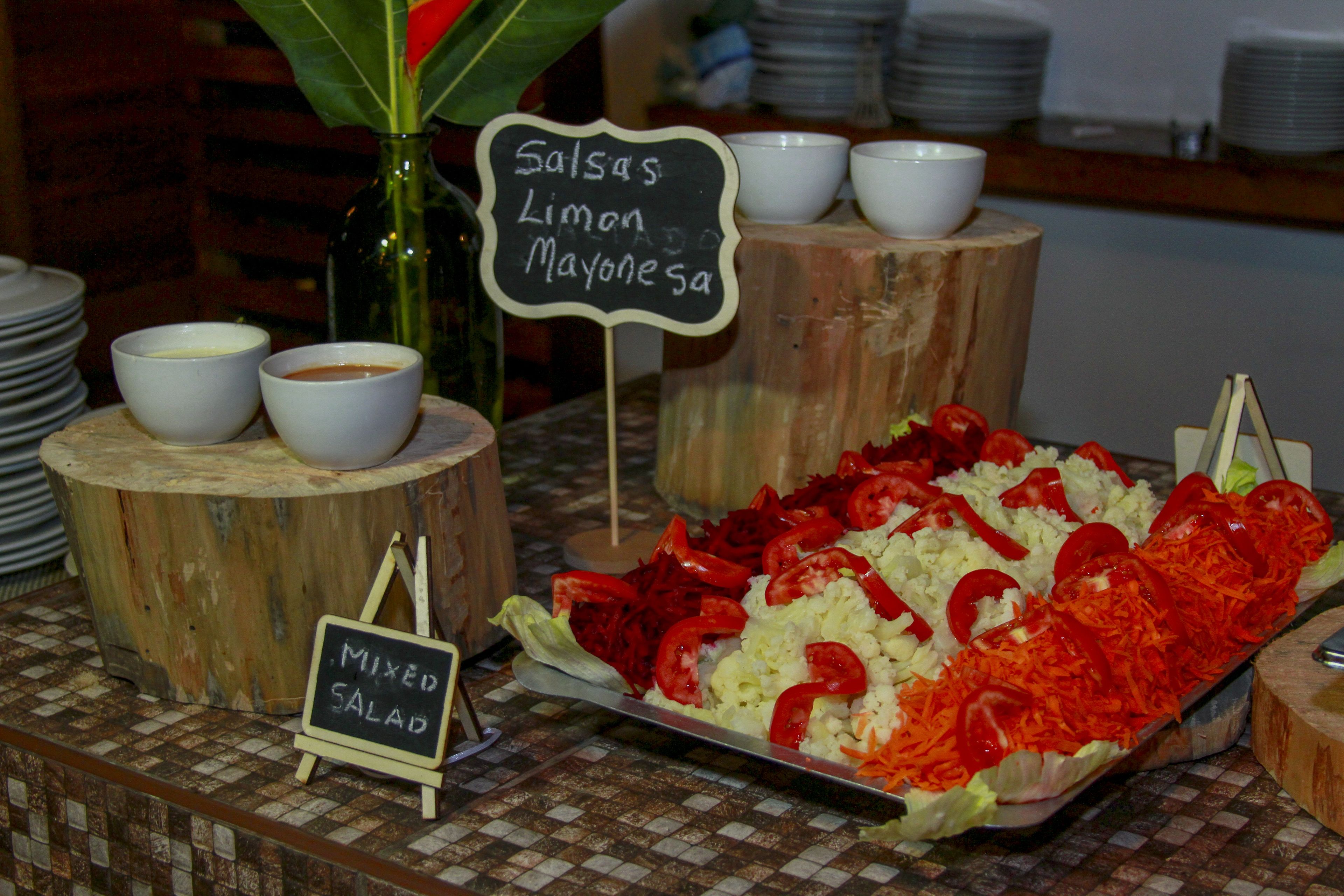 A buffet table with labeled dishes including 'Salsas', 'Limon', 'Mayonesa', and 'Mixed Salad'.
