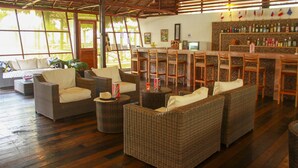 A spacious lounge area with wicker furniture, a bar, and large windows. - Heliconia Amazon River Lodge (Indiana)