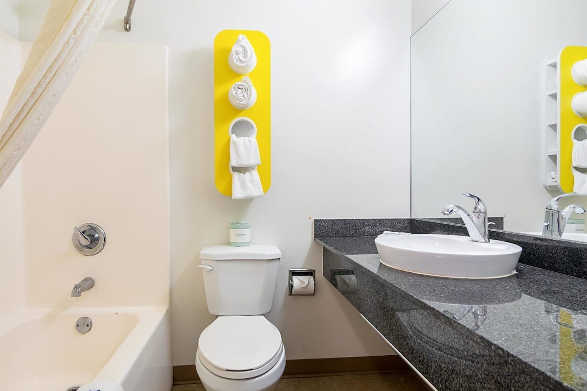 A bathroom with a bathtub, toilet, and sink. There is a yellow towel rack with towels and a toilet paper holder.