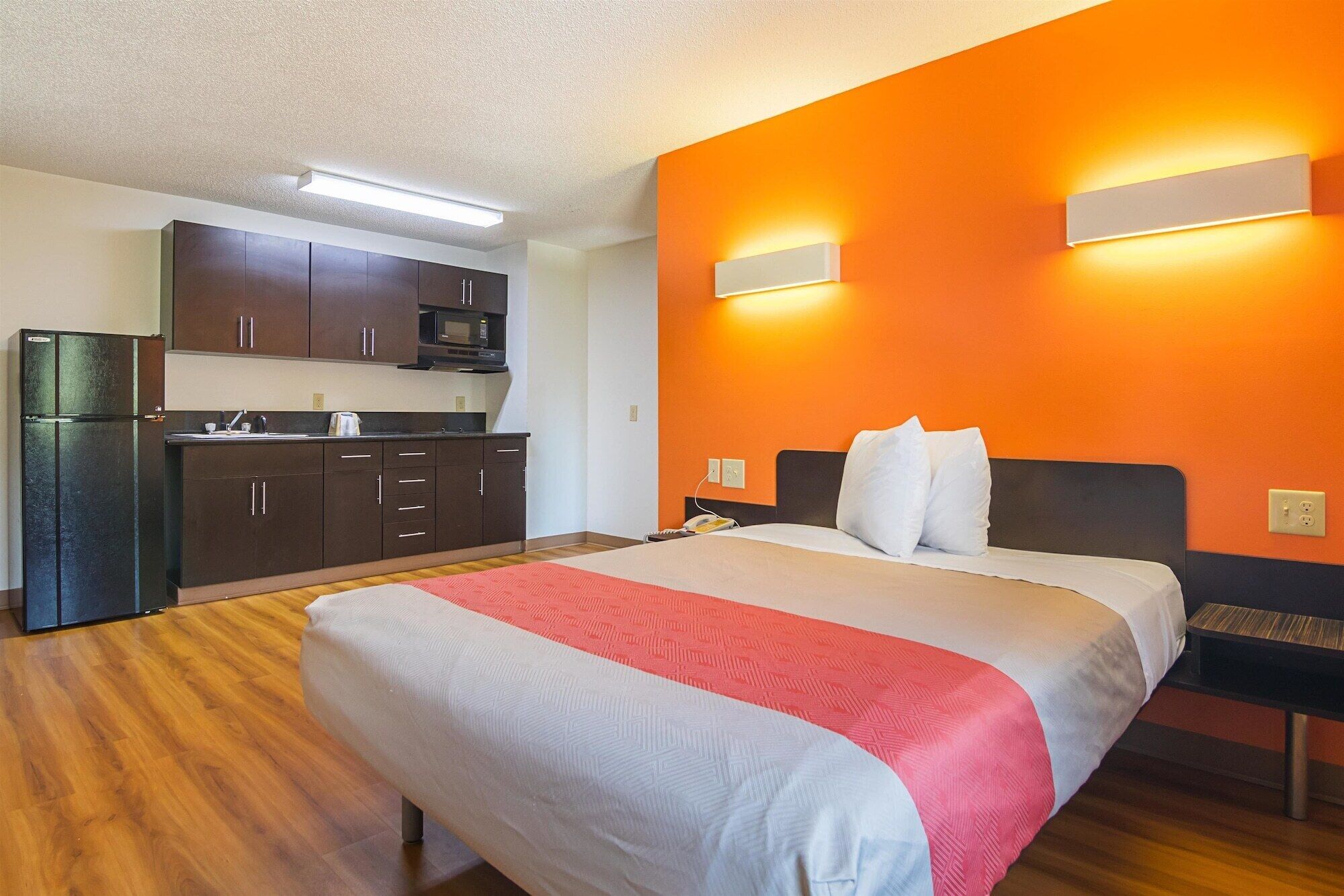 A hotel room with a bed, a kitchenette, and orange walls.