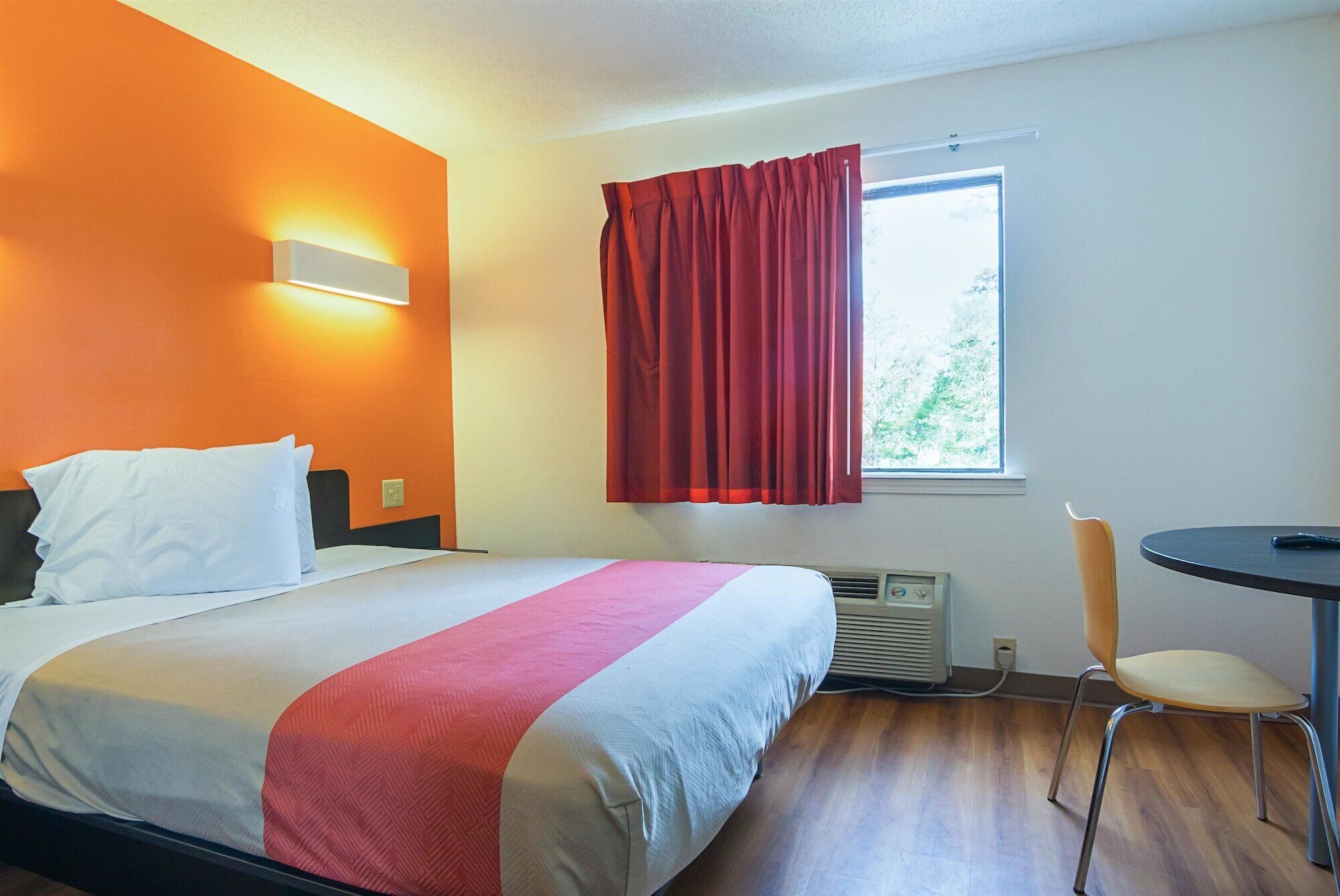 A hotel room with a bed, a chair, a table, and a window with curtains.
