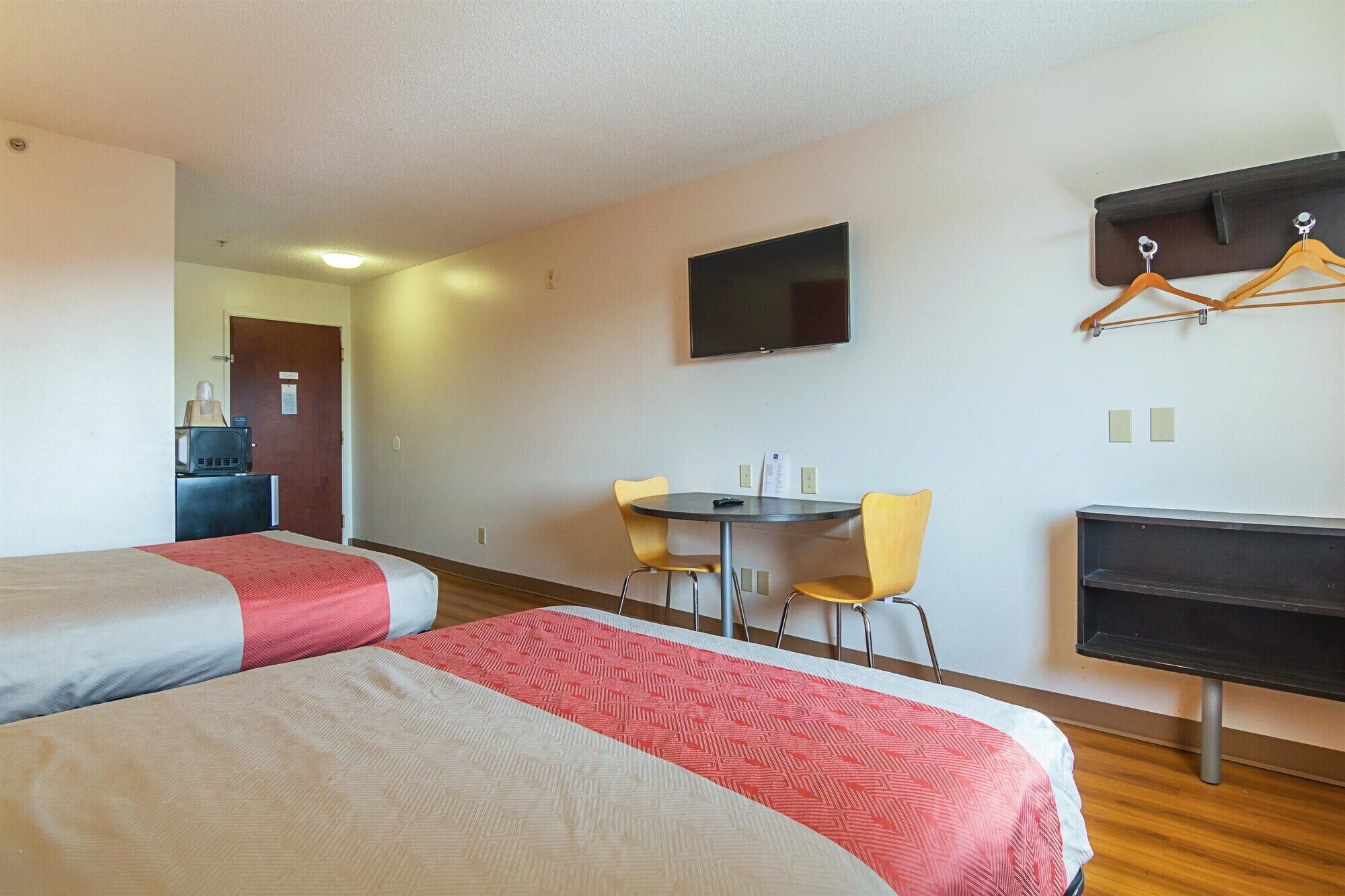Una habitación de hotel con dos camas, un escritorio, una silla, un televisor y un perchero.