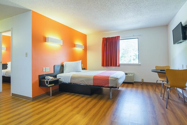 A hotel room with a bed, bedside table, chair, window, and a TV on the wall. - Motel 6 Jonesboro, GA (Jonesboro)