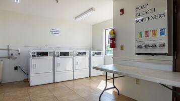 A laundry room with four white washers and dryers, a table, and a wall sign advertising soap, bleach, and softeners.