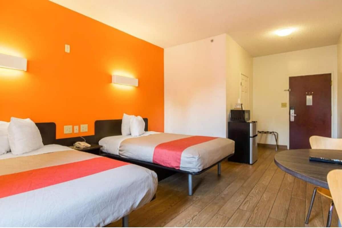 A hotel room with two beds, a desk, a chair, and a small table.