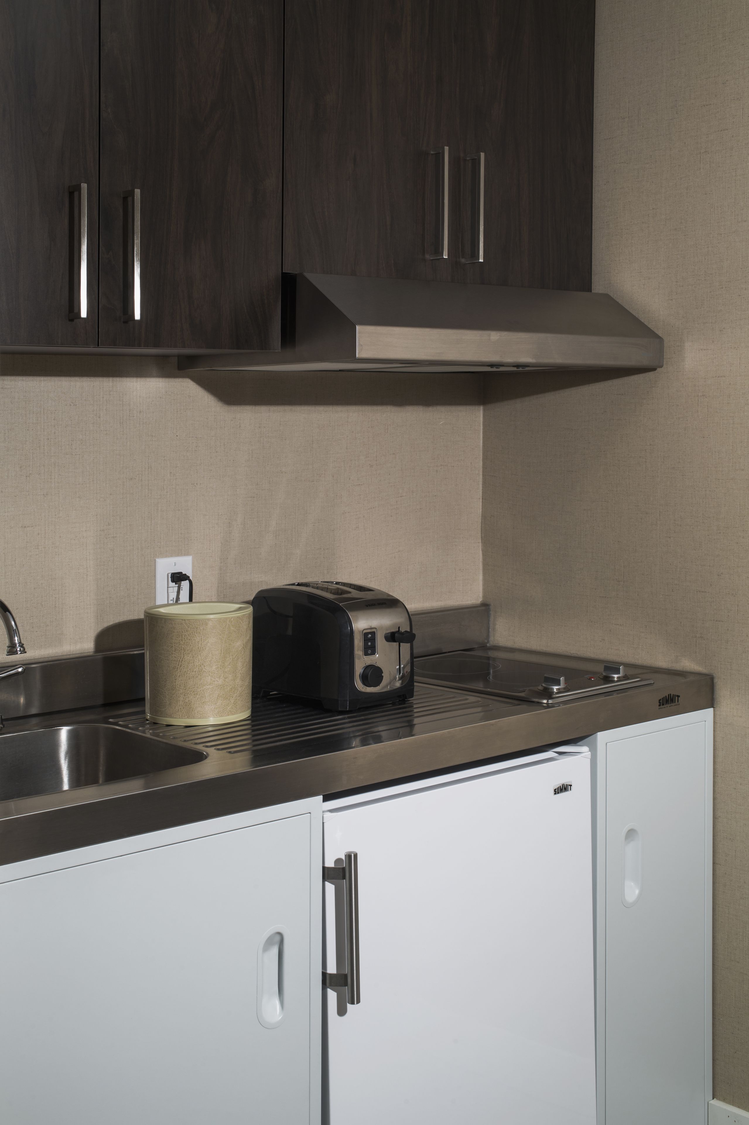 Una cocina con armarios de madera oscura, una campana extractora de acero inoxidable, un tostador y un refrigerador blanco.