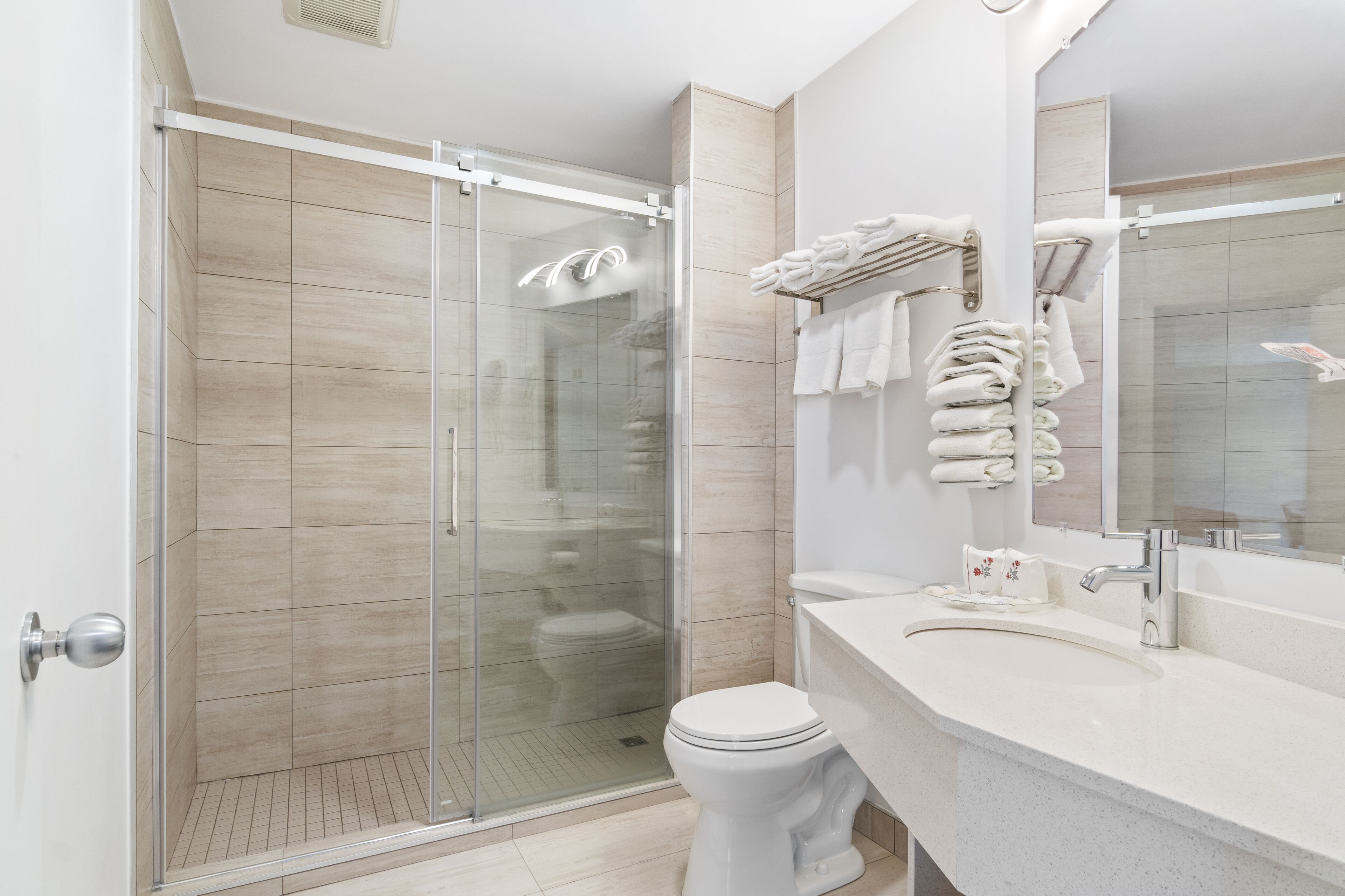 A modern bathroom with a glass-enclosed shower, a white toilet, and a vanity with a mirror and towel rack.