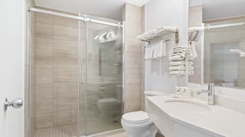 A modern bathroom with a glass-enclosed shower, a white toilet, and a vanity with a mirror and towel rack.