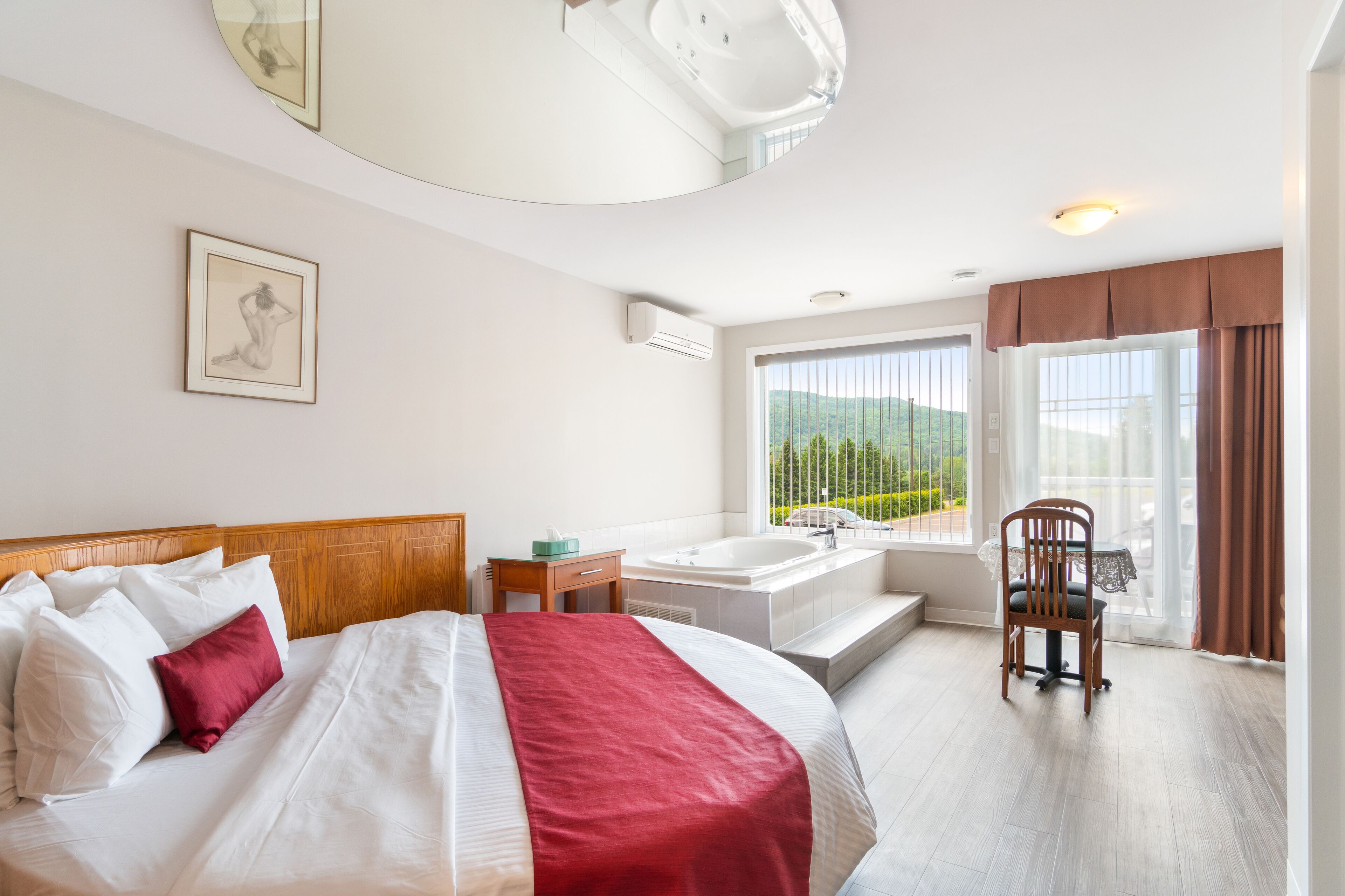 Ett hotellrum med en stor säng, en sittgrupp med en fåtölj, ett badkar och utsikt över grönområden genom fönstret.
