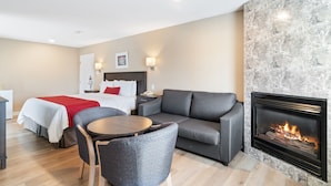 A modern hotel room with a fireplace, a sofa, a dining table, and a bed with red pillows. - Hotel Bromont (Bromont)