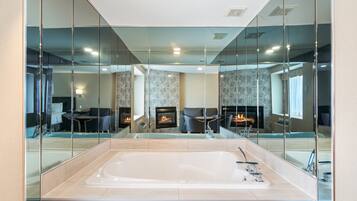 Un baño moderno con una bañera grande, una chimenea y una zona de estar visible a través de un mamparo de cristal.