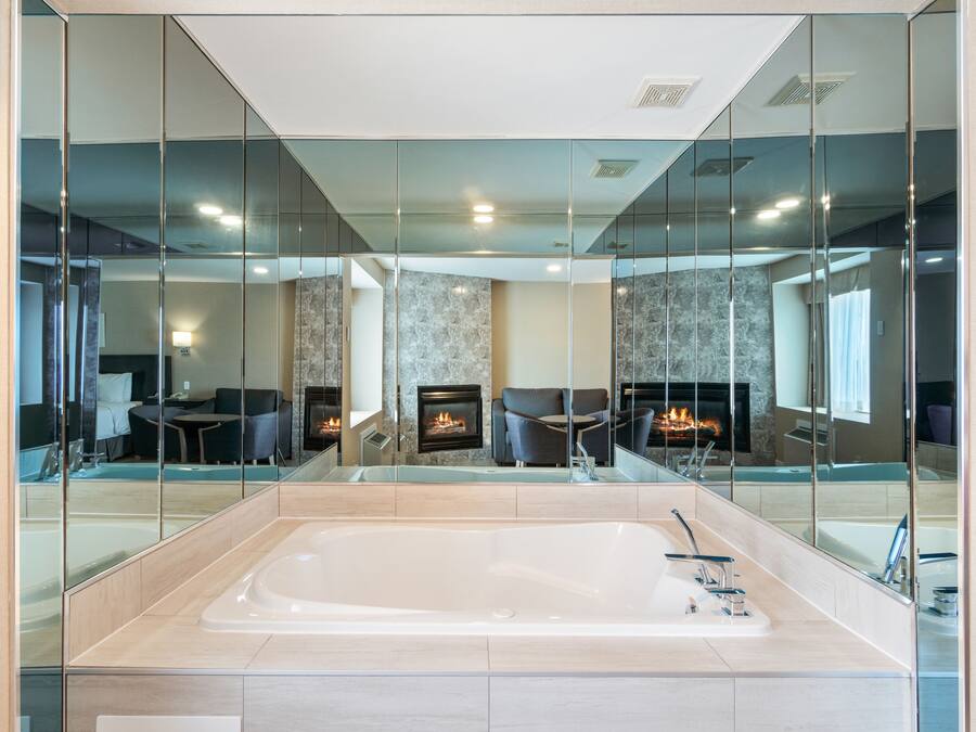 A modern bathroom with a large bathtub, a fireplace, and a seating area visible through a glass partition.