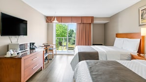 A hotel room with a large flat-screen TV, a desk with a coffee maker, and a bed with a headboard. - Hotel Bromont (Bromont)